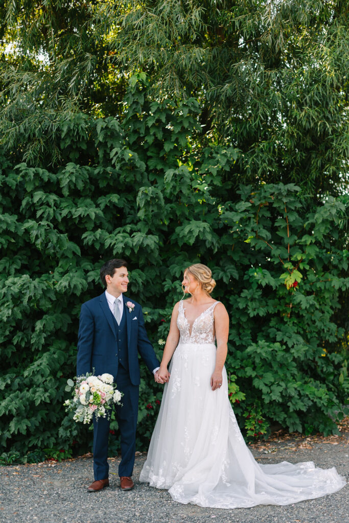 bride and groom standing in front of green foliage on wedding day