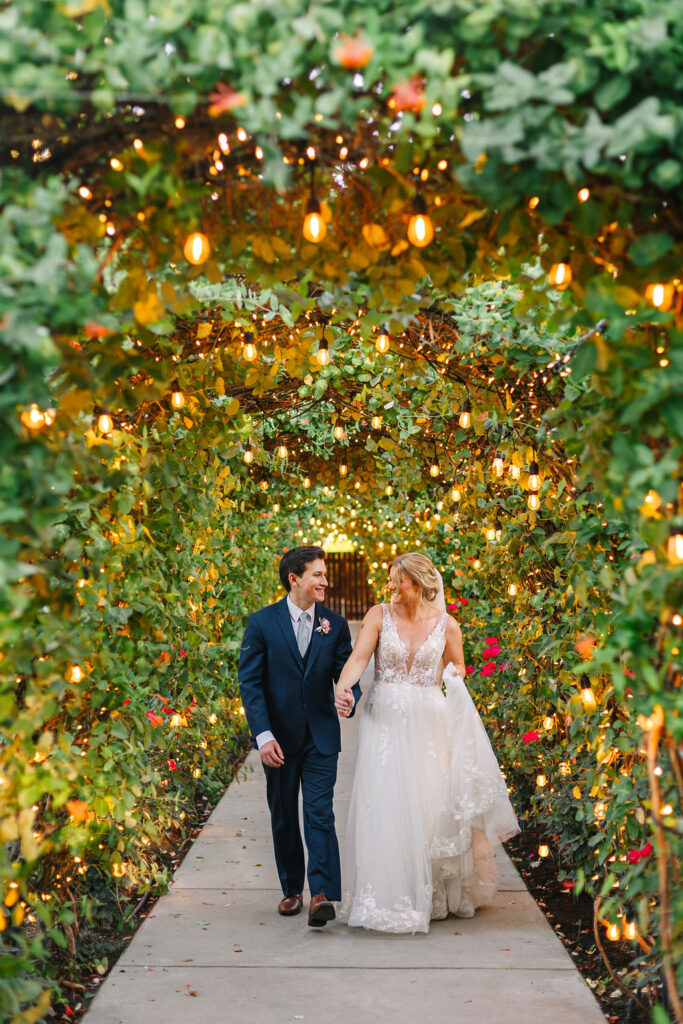 bride and groom walking together under lighted archway hand in hand