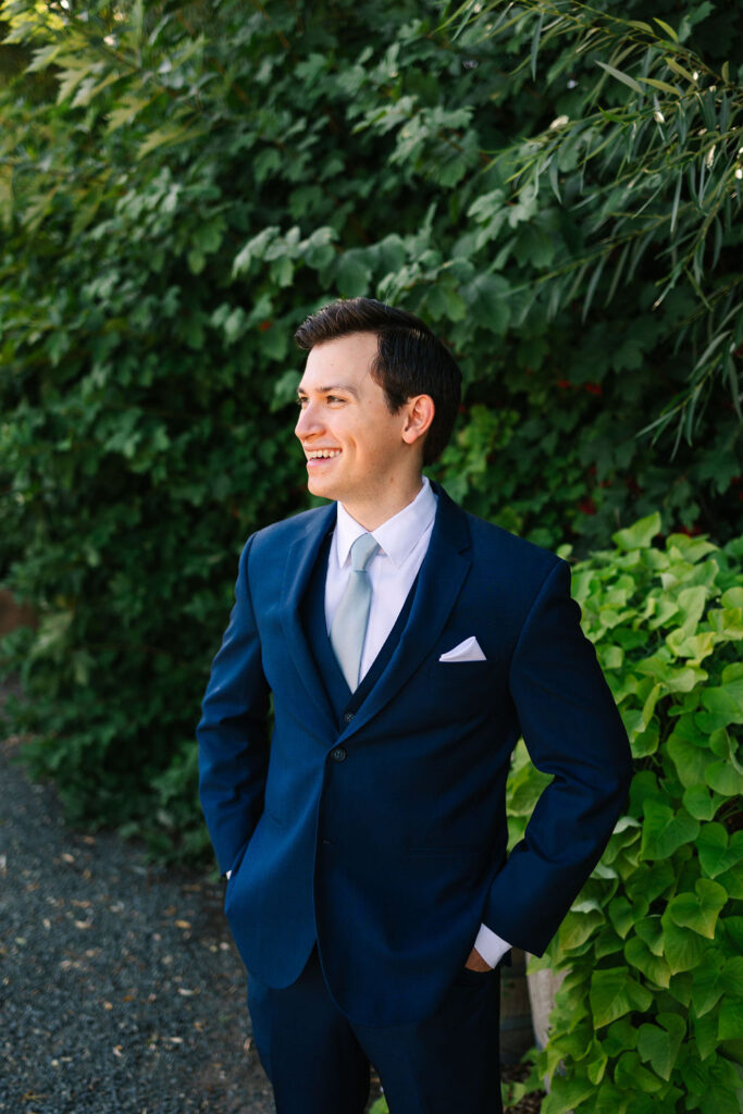 groom in wedding attire in front of green foliage