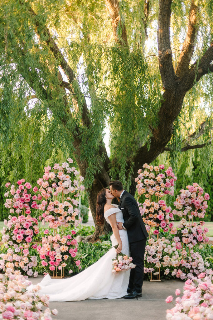 couple kissing in front of a colorful pink floral installation. find ideas for your tri-cities wedding venues