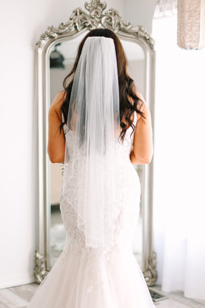 bride stands in front of a vintage mirror in her wedding gown